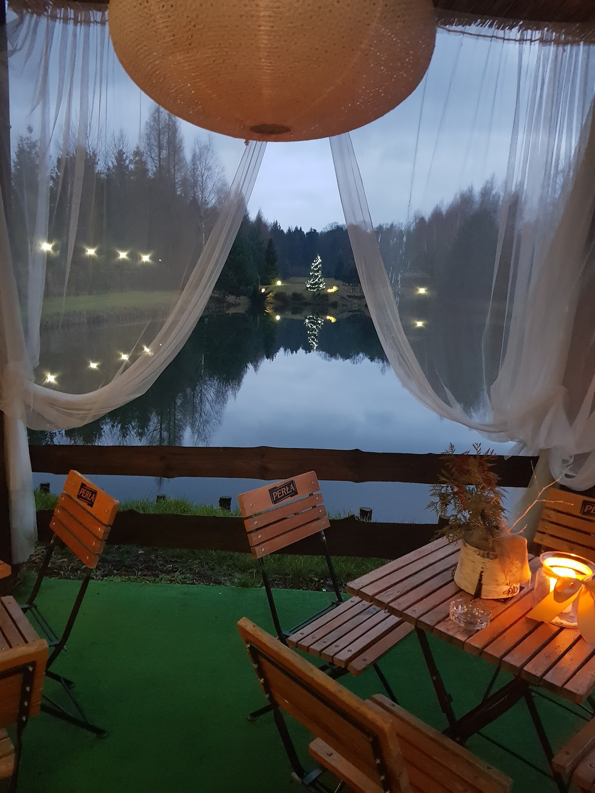Taras nad stawem o zmierzchu - lampion, drewniane meble, widok na taflę wody